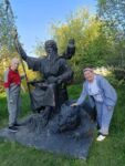 На фотографии изображены два человека, стоящие рядом со скульптурной композицией.Скульптура представляет собой сидящего бородатого старца.
