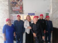 На фотографии группа из шести человек,среди которых один мужчина и пять женщин,стоят в фойе кинотеатра.Все они в повседневной одежде,некоторые из них носят красные бейсболки с надписью «Волонтер».
